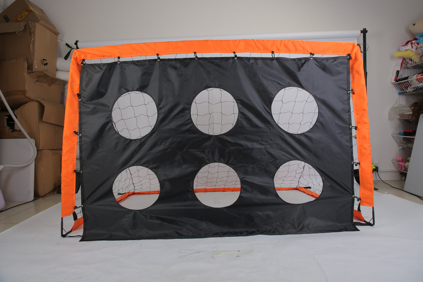 Small soccer goal with orange frame and gray backrest on a white floor.