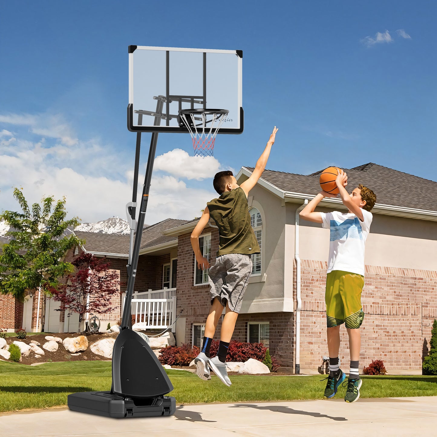 Two children playing basketball in front of a adjustable outdoor hoop.