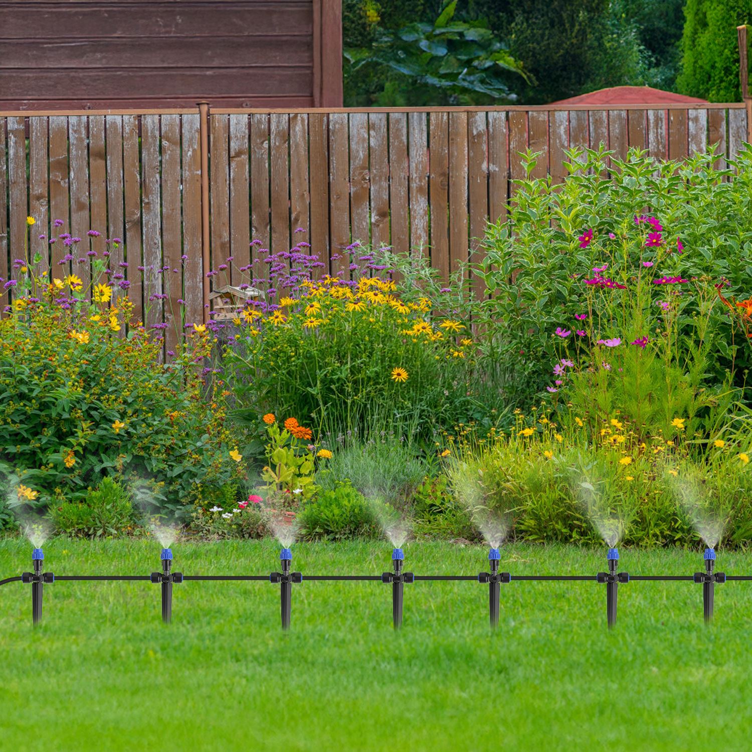 Sprinklers watering a garden with a wooden fence and plants in the background