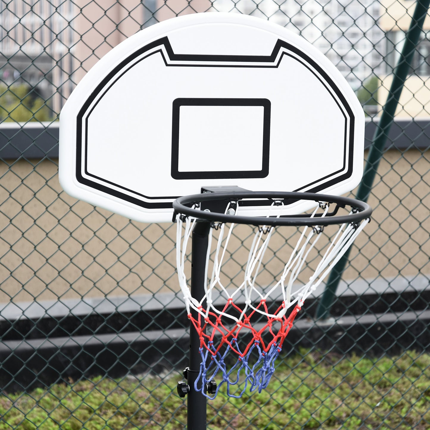 Basketball hoop with a white backboard and red and blue rim against a chain-link fence.